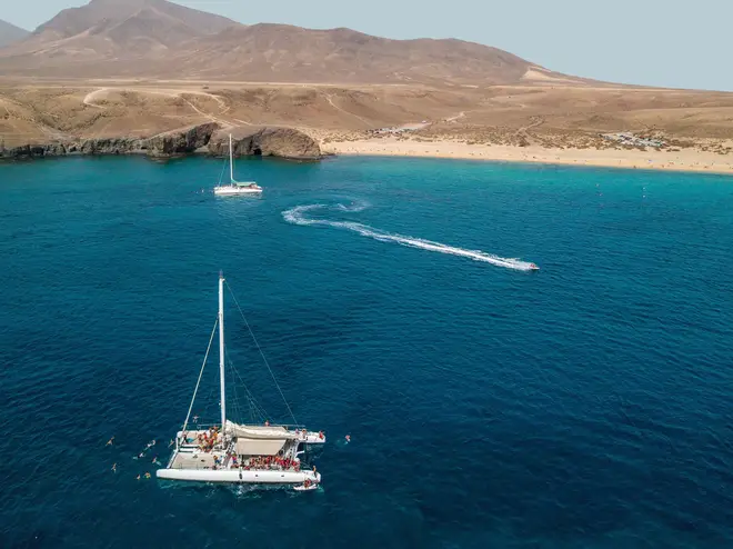 Aerial view of a catamaran with people on board and in the sea, swimming near the coasts of the island of Lanzarote, Canary, Spain. Jet ski